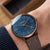 Montre pour homme au poignet avec cadran bleu et bracelet en cuir marron foncé.