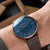 Montre pour homme au poignet : cadran bleu, bracelet en cuir marron, lunette or rose