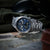 Herren-Chronographuhr mit blauem Zifferblatt und Edelstahlarmband auf dunkler Oberfläche