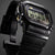 Casio G-Shock Herrenuhr schräg, schwarzes Titan-Optikgehäuse mit goldenen Akzenten.