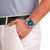 Am Handgelenk: Herrenuhr mit blauem Zifferblatt, Chronograph und silbernem Gehäuse am blauem Band