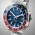 Edelstahl-Herrenarmbanduhr in schräger Ansicht: blaues Zifferblatt, rote/blaue GMT-Lünette und Krone