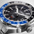 Gros plan d'une montre pour homme : cadran noir avec index blancs et aiguille GMT