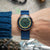 Montre pour homme avec cadran vert, boîtier couleur or rose et bracelet en tissu bleu