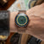 Montre pour homme au poignet avec bracelet en métal couleur or rose et cadran vert