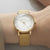 Montre dorée pour femme au poignet, cadran blanc et bracelet milanais