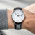 Montre-bracelet au poignet : bracelet en cuir noir, boîtier argenté, cadran blanc