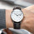 Montre avec bracelet en cuir marron et cadran blanc, aiguilles fines et guichet date.