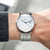 Montre avec bracelet en métal argenté et cadran blanc, aiguilles fines et guichet date.