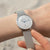 Montre pour femme au poignet avec bracelet en maille argentée et cadran blanc, aiguilles bleues