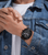 Am Handgelenk getragene Herrenuhr mit schwarzem Armband auf Jeanshemd, Ziffernblatt sichtbar.
