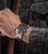 Herrenuhr am Handgelenk mit silbernem Metallarmband am Ärmel einer Jeansjacke