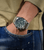 Herrenarmbanduhr am Handgelenk mit silbernem Metallarmband und grünem Zifferblatt