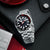 Herrenuhr mit schwarzem Zifferblatt, silbernem Armband, roter Markierung und Krone