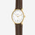 Montre homme de face : boîtier rond doré, cadran blanc, bracelet en cuir marron.