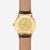 Dos de la montre homme : boîtier doré avec gravure, bracelet en cuir marron.
