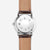 Fond de montre Sternglas pour homme avec design circulaire dans un boîtier argenté, bracelet en cuir marron.