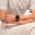 Schwarze Swatch Armbanduhr am Handgelenk auf hellem Stoff, rundes Zifferblatt