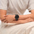 Schwarze Swatch Armbanduhr am Handgelenk, rundes Gehäuse mit dunklem Zifferblatt