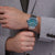 Herrenarmbanduhr am Handgelenk mit blau-grünem Zifferblatt und Metallband