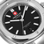 Nahaufnahme Herrenarmbanduhr: schwarzes Zifferblatt, rote Swiss-Marke, Stabindexe und Datum „28“