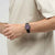 Dunkelbraune Armbanduhr am Handgelenk mit rundem violettem Zifferblatt und „FRI 28“