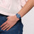 Damenarmbanduhr am Handgelenk: rundes blaues Zifferblatt, dunkelblaues Armband an Jeans.
