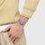 Swatch-Armbanduhr am Handgelenk mit transparentem Gehäuse und farbigem Zifferblatt