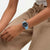 Hellblaue Armbanduhr am Handgelenk mit schwarzem Zifferblatt und weißen Leuchtzeigern.