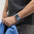 Hellblaue Armbanduhr am Handgelenk mit schwarzem Zifferblatt und silbernem Rahmen.