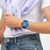 Swatch Armbanduhr blau am Handgelenk, gestreiftes Zifferblatt und orangefarbene Zeiger