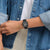 Schwarze Armbanduhr am Handgelenk mit rechteckigem Zifferblatt, an Jeansjacke getragen