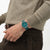 Armbanduhr am Handgelenk mit dunkelgrünem Zifferblatt, gebürstetem Edelstahlgehäuse und grünem Band