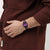 Swatch Damenuhr am Handgelenk: violettes Zifferblatt, schwarzes Armband mit violettem Muster