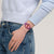 Swatch Uhr am Handgelenk: lila Armband mit korallenfarbenem Zifferblatt und blauen Markierungen