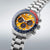 Herren-Armbanduhr 3/4-Ansicht mit Stahlarmband, orangefarbenem Zifferblatt und roter/blauer Lünette