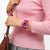 Fuchsia Armbanduhr am Handgelenk neben braunem Riemen, am pinken Strickpullover