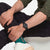 Chronograph am Handgelenk mit blauem Kunststoffarmband auf dunkler Hose.