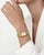 Damen-Armbanduhr am Handgelenk mit goldfarbenem Metallarmband und rechteckigem Zifferblatt