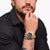 Armbanduhr am Handgelenk mit schwarzem Zifferblatt, goldfarbenem Metallband und Chronograph