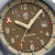 Détail du cadran d'une montre de sport : affichage beige, aiguilles argentées, guichet date à 31