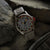 Montre homme avec boîtier beige, bracelet gris texturé et détails orange sur le cadran