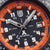 Zifferblattdetail einer Herrenarmbanduhr: orange Rand, Leuchtmarkierungen und Datum