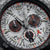 Gros plan : cadran argenté avec trois sous-cadrans de chronographe et des index orange.
