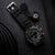 Montre bracelet pour homme sur bracelet noir avec chiffres luminescents ; à côté, petit accessoire boussole.