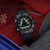 Montre homme au poignet, boîtier noir, chiffres lumineux verts et bracelet textile noir