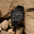 Montre pour homme sur des rochers : cadran noir, aiguilles argentées et bracelet noir