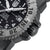 Gros plan d'une montre pour homme sur le côté : lunette moletée, couronne robuste et bouton poussoir sombre sur le bracelet.