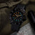 Montre pour homme au poignet avec bracelet noir et chiffres luminescents sur cadran sombre.