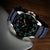 Montre homme de côté : bracelet bleu foncé, boîtier en acier inoxydable et aiguilles lumineuses sur le cadran.